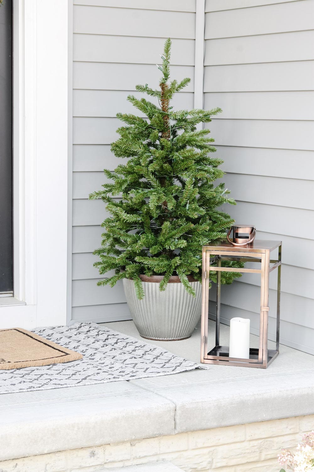 A plain porch tree is styled next to bronze lantern with candle