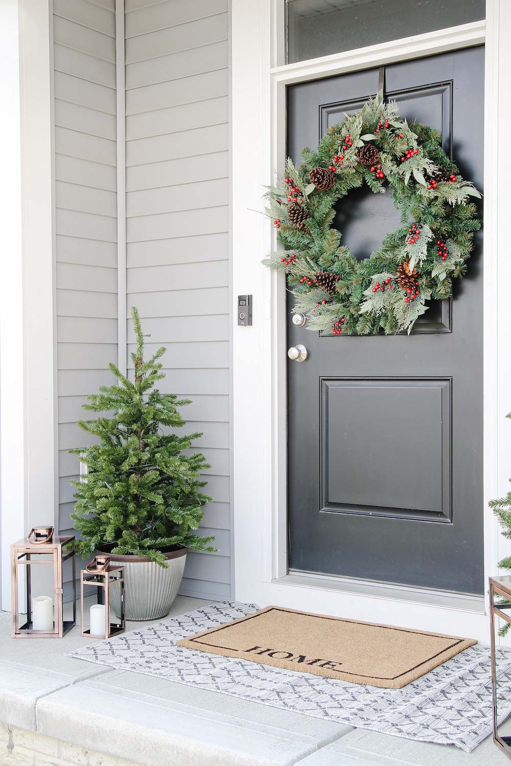 A front porch styled for the holidays with door wreath, porch trees and lanterns