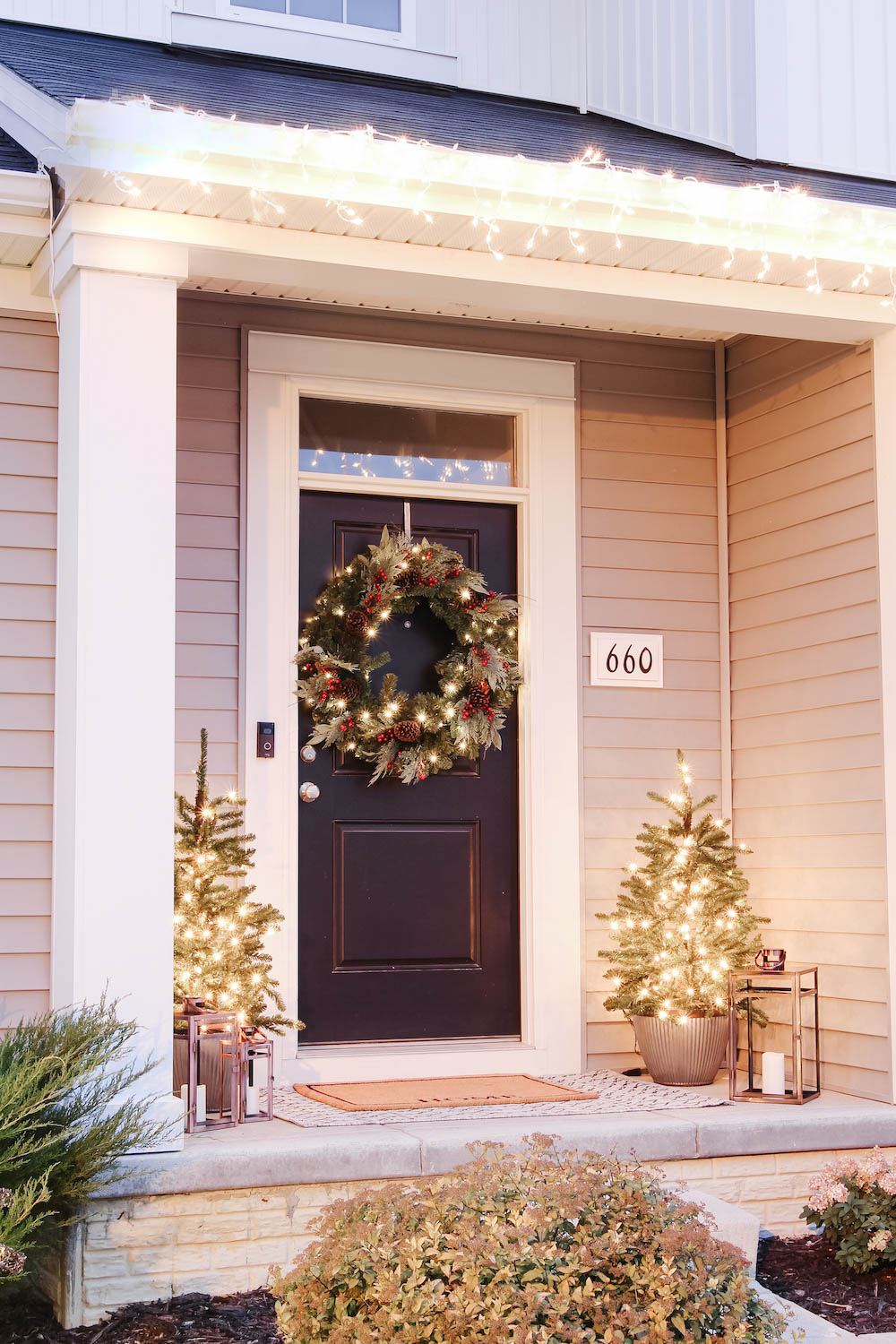 A front porch styled at night with oversized wreath and porch trees lit