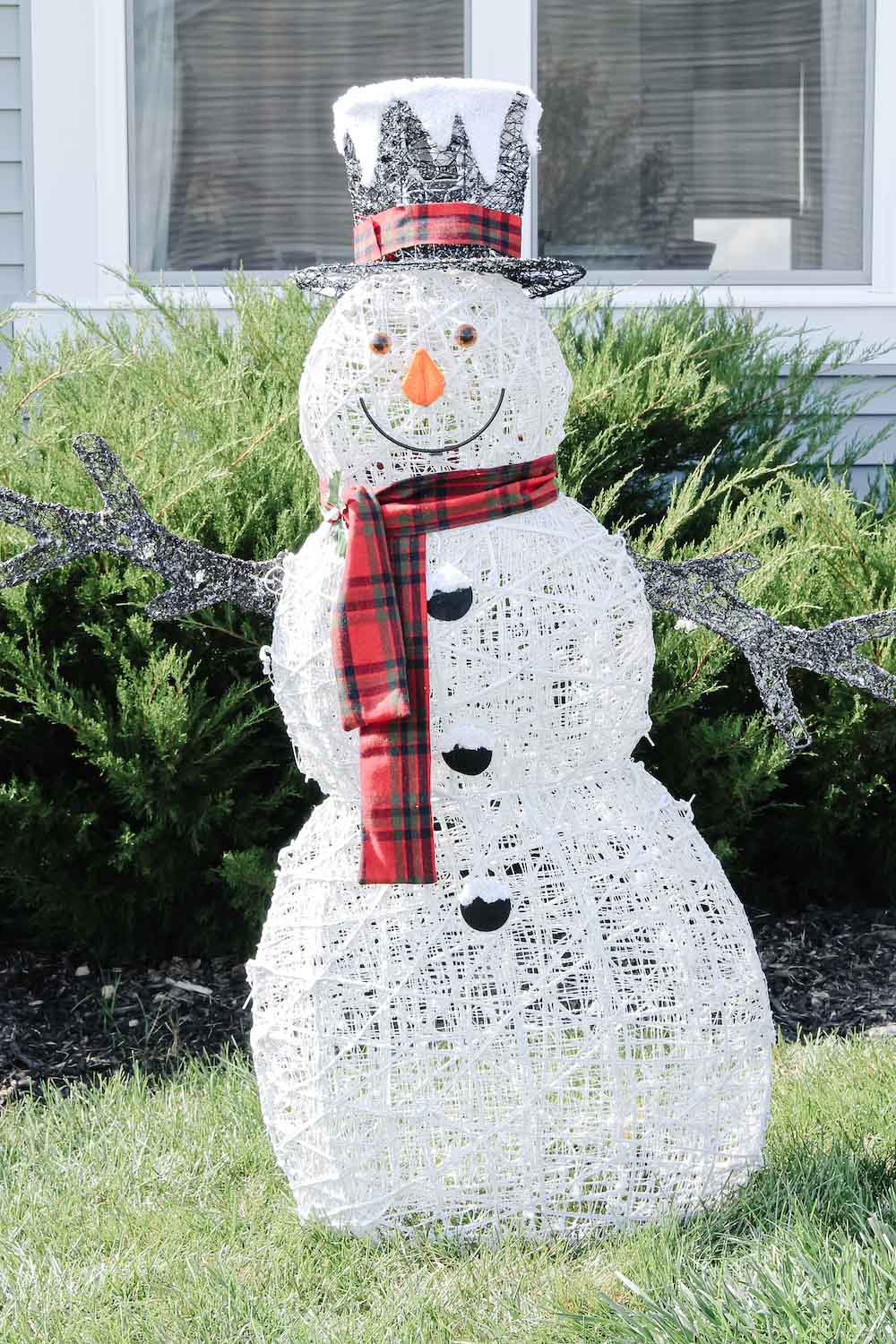 Outdoor holiday snowman with red scarf and matching hat in front yard during day