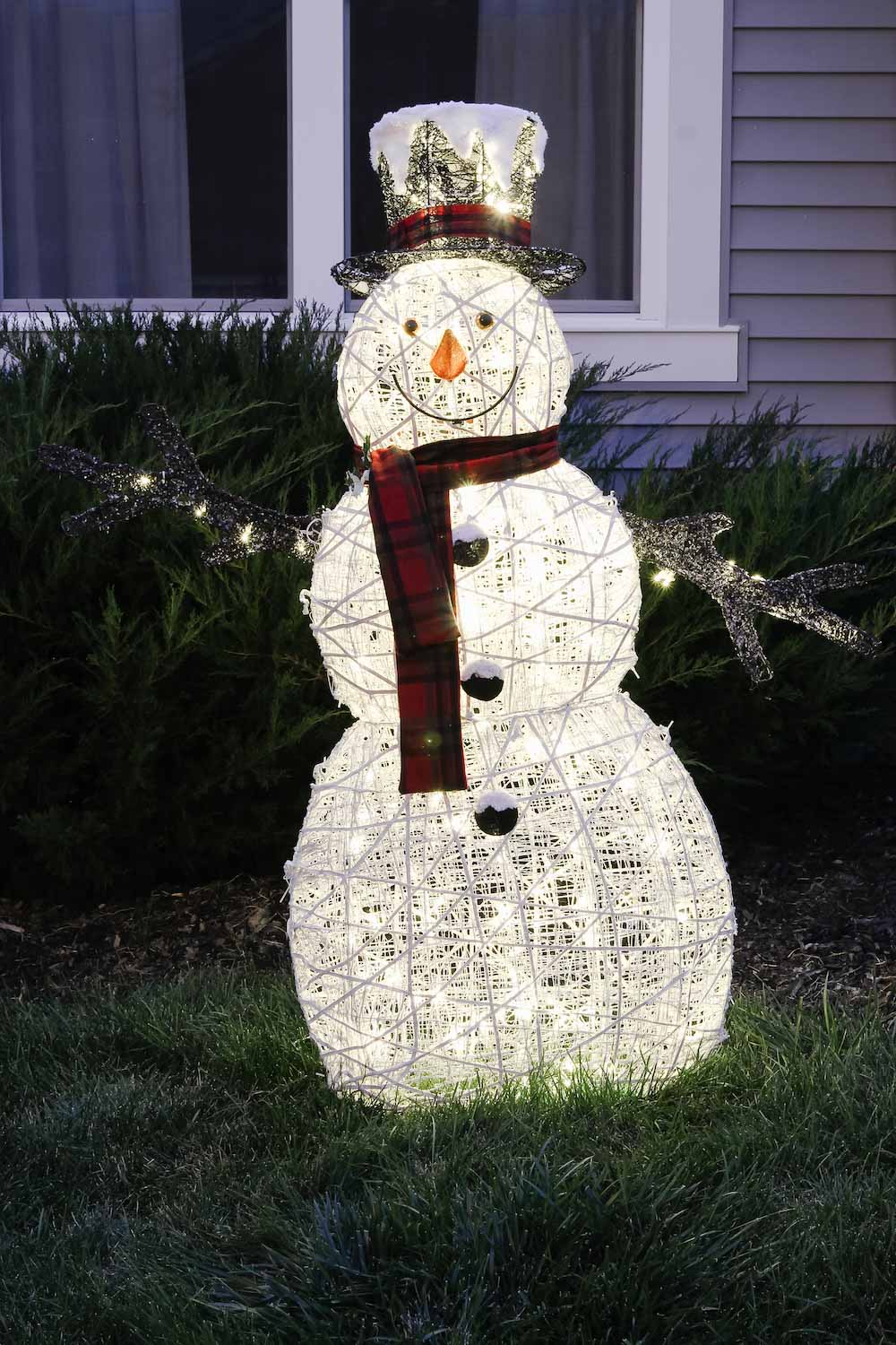 Outdoor holiday snowman with red scarf and matching hat in front yard at night