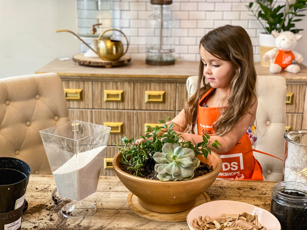 Picture of a little girl behind a terra cotta bowl of ferns and succulents
