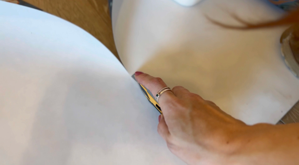 A woman’s hand using a utility knife to cut wallpaper.