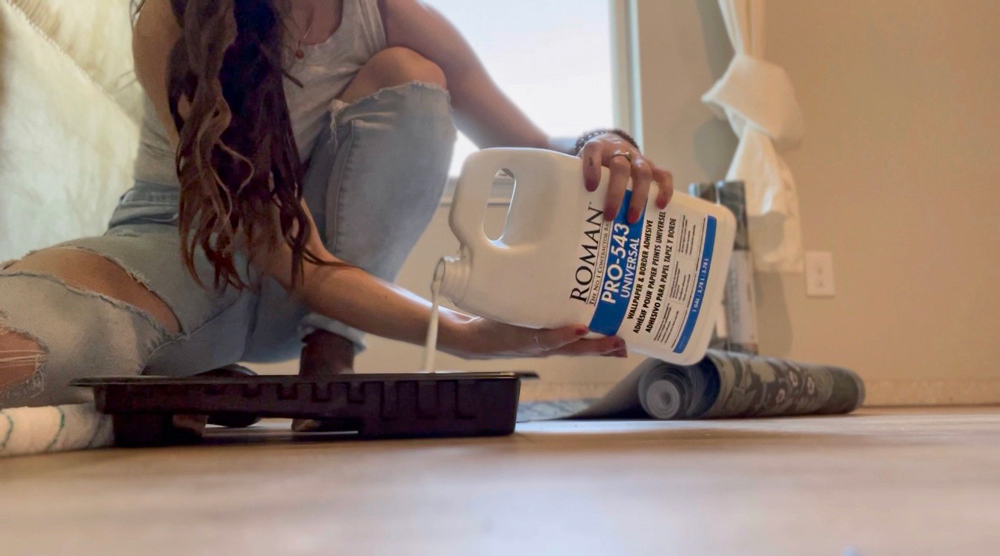 A woman sitting on the floor pouring wallpaper paste into a paint tray