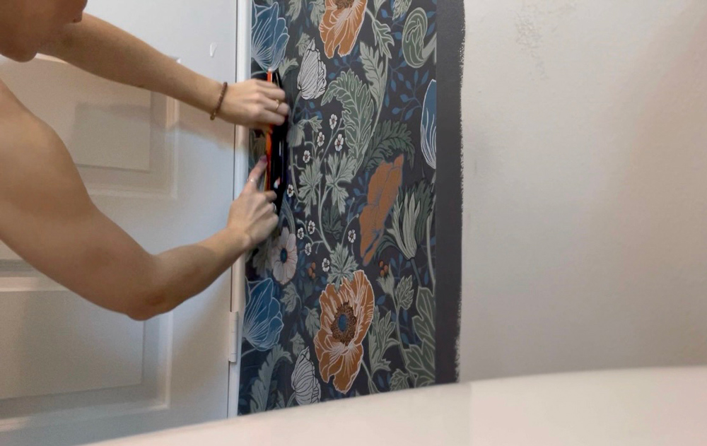 A woman smoothing the corner of wallpaper with a smoothing tool.