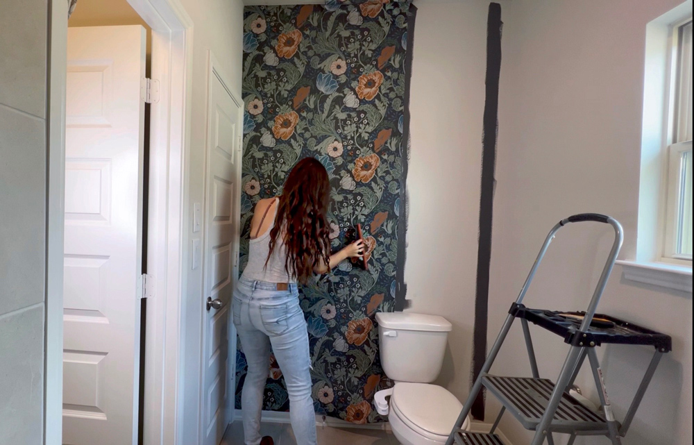 A woman smoothing out a sheet of wallpaper on a wall.