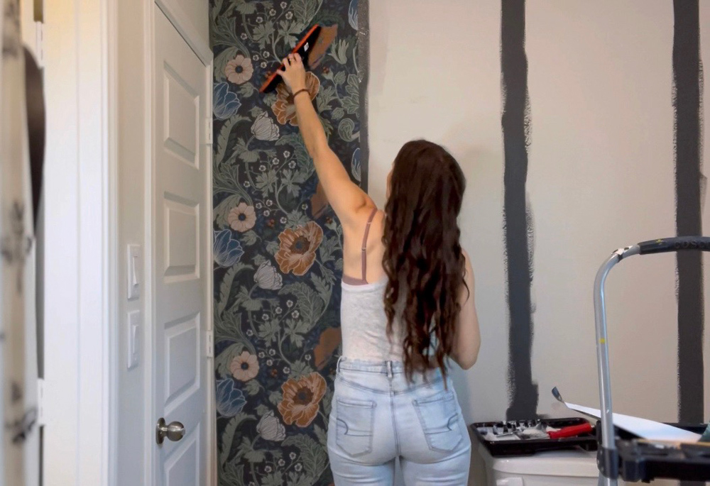 A woman flattening wallpaper on a wall with a smoothing tool.