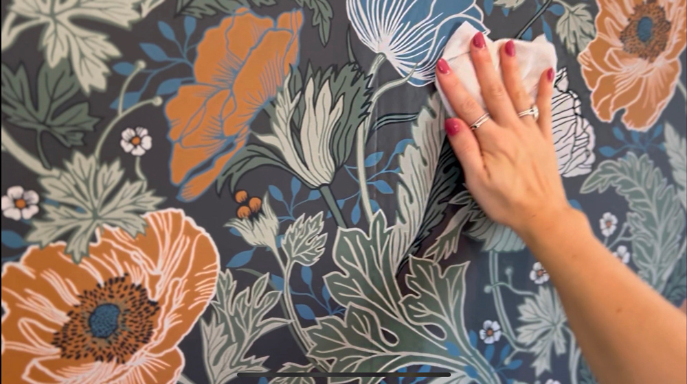 A woman’s hand smoothing wallpaper onto a wall.