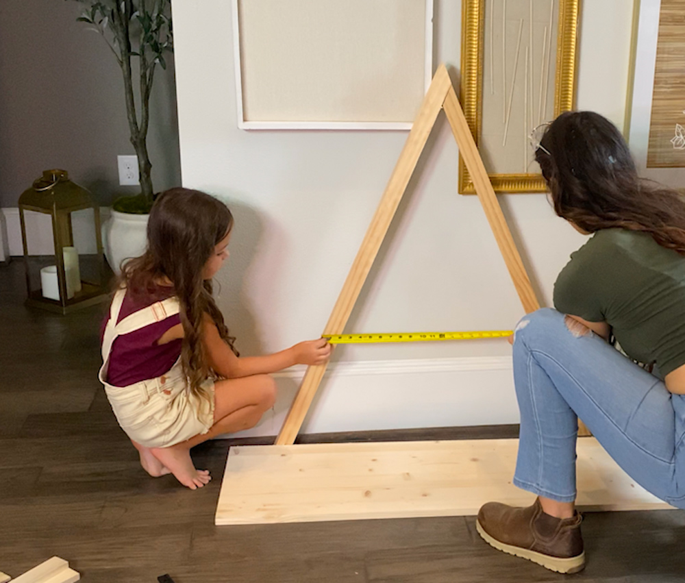 A woman and a child holding a tape measure across a triangular wooden frame