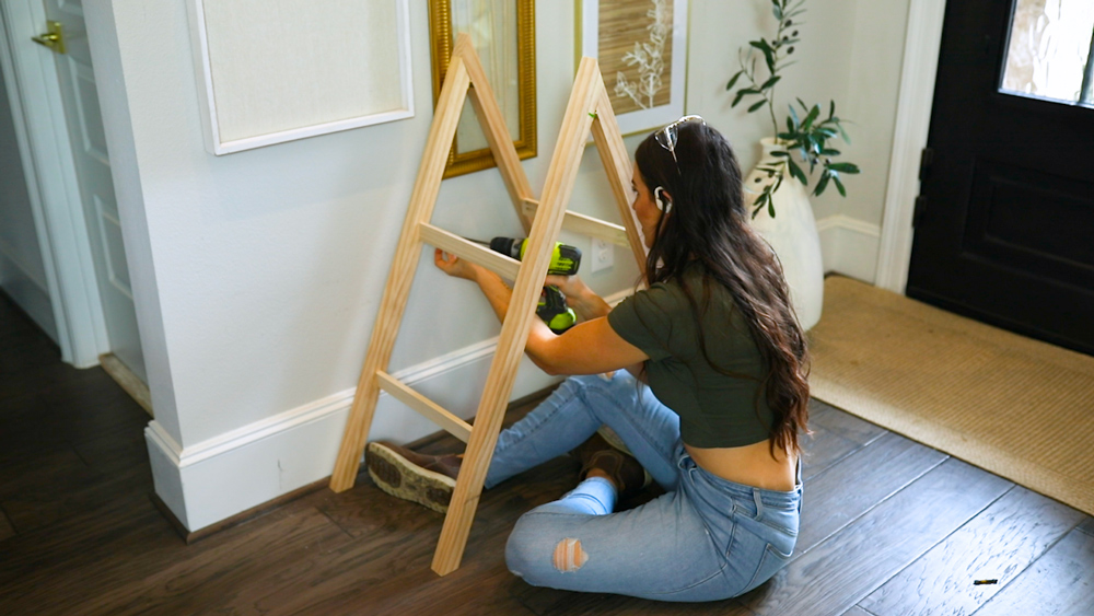 A woman using a drill to attach side supports on a DIY present ladder
