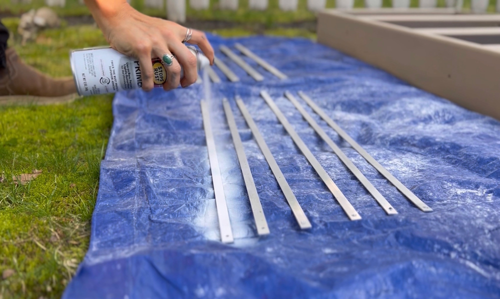 A woman spray painting aluminum bars with primer.