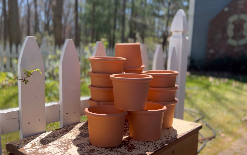Several small terracotta pots on a table next to a white picket fence.
