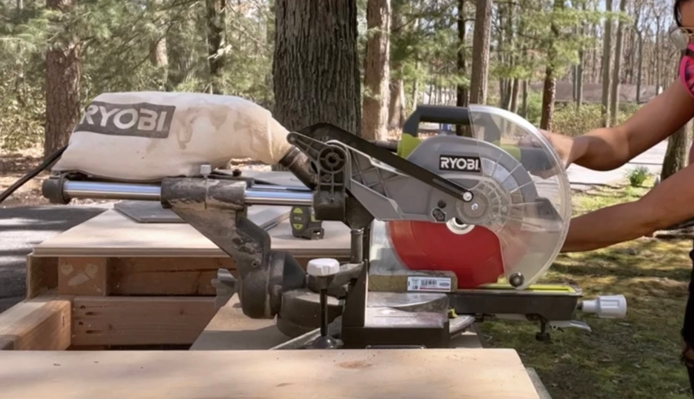 A woman using a RYOBI miter saw to cut the end of a wooden board.
