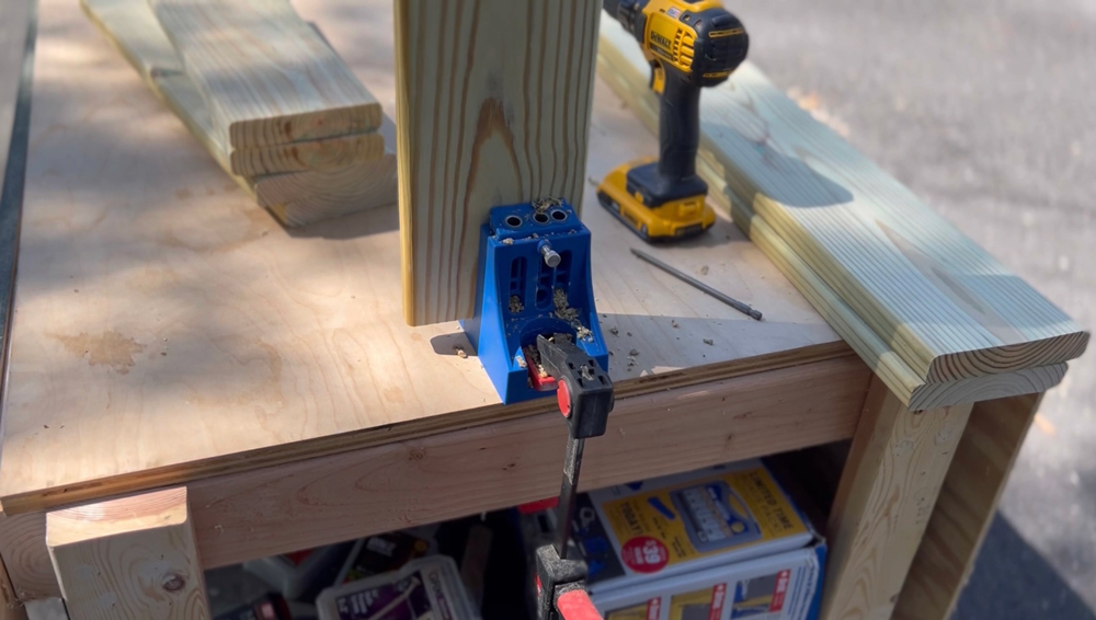 A kreg pocket hole jig being held on a board by a clamp on a table.