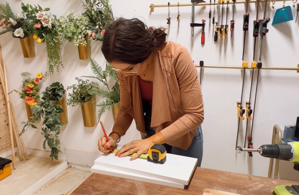 A woman using a tape measure to measure a set of boards.