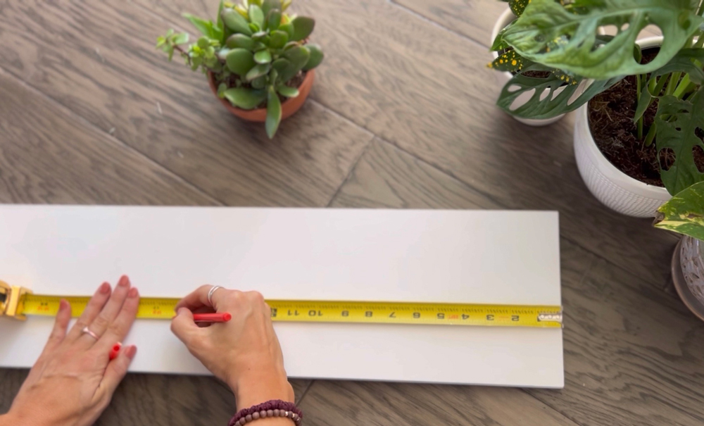 A woman’s hands marking a white board using a measuring tape.