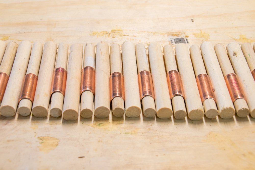 Wooden dowels with copper piping attached laying out on a wooden surface. 