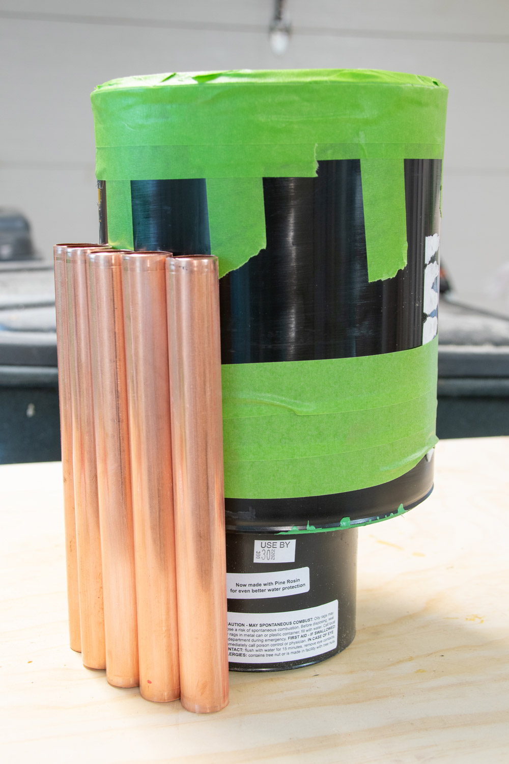 A tape-wrapped paint can sitting on a small paint can with copper piping resting against it. 