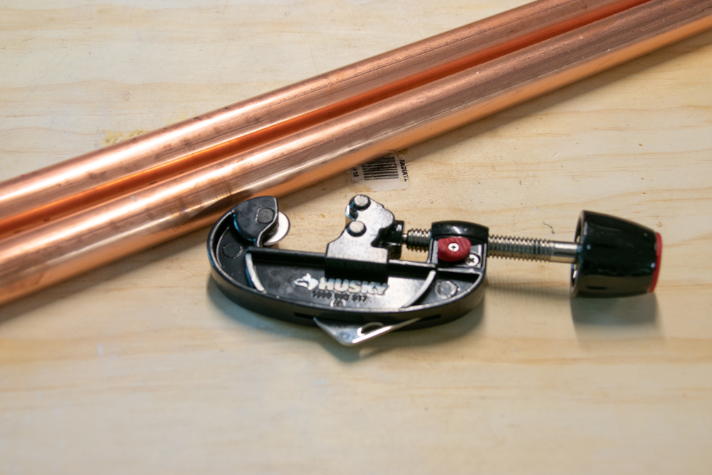 A pipe cutter lying next to two rods of copper piping.