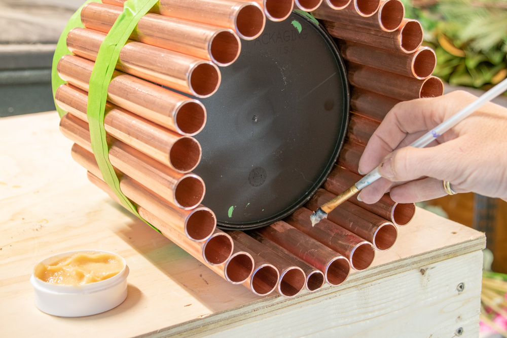 A paint can surrounded by copper piping being painted with flux.