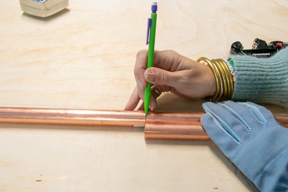 A hand drawing marks on copper piping using a mechanical pencil.