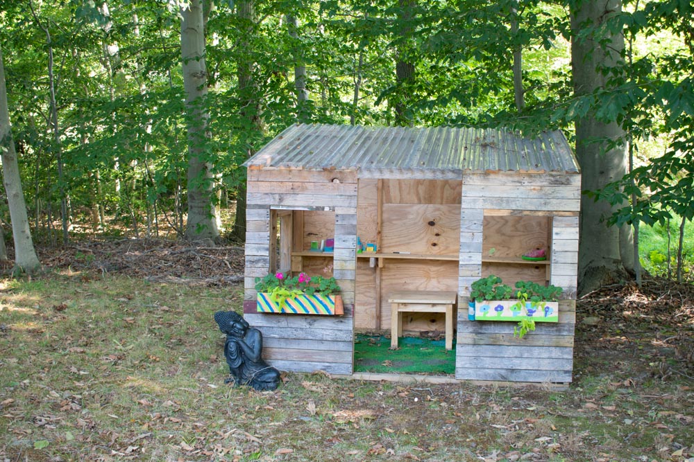 A wooden playhouse with window boxes sitting in the woods.