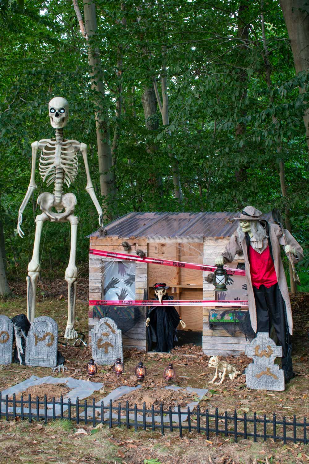 A scary Halloween graveyard guarded by a Victorian reaper, giant skeleton, and a gravedigger with his skeleton dog.