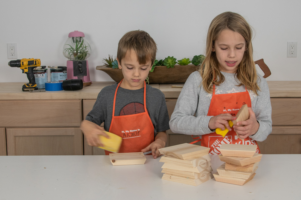  A boy and a girl using sanding blocks on pre-cut wooden pieces.