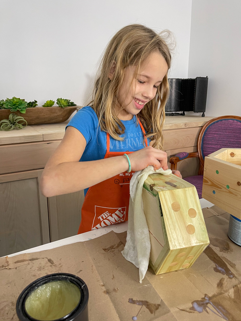 A young girl applying furniture wax to an unfinished hexagonal planter.