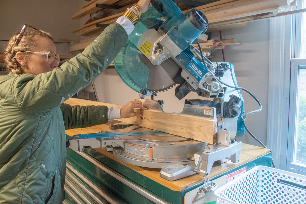 An adult woman using a table saw to cut a wooden board.