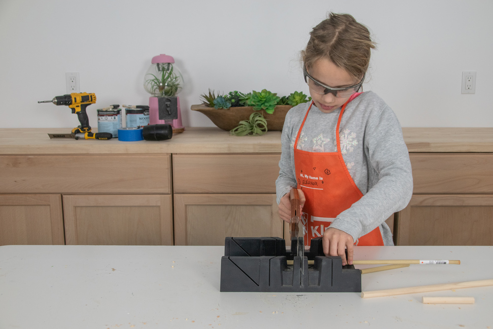 A young girl using a saw guide and a hand saw to cut dowels.
