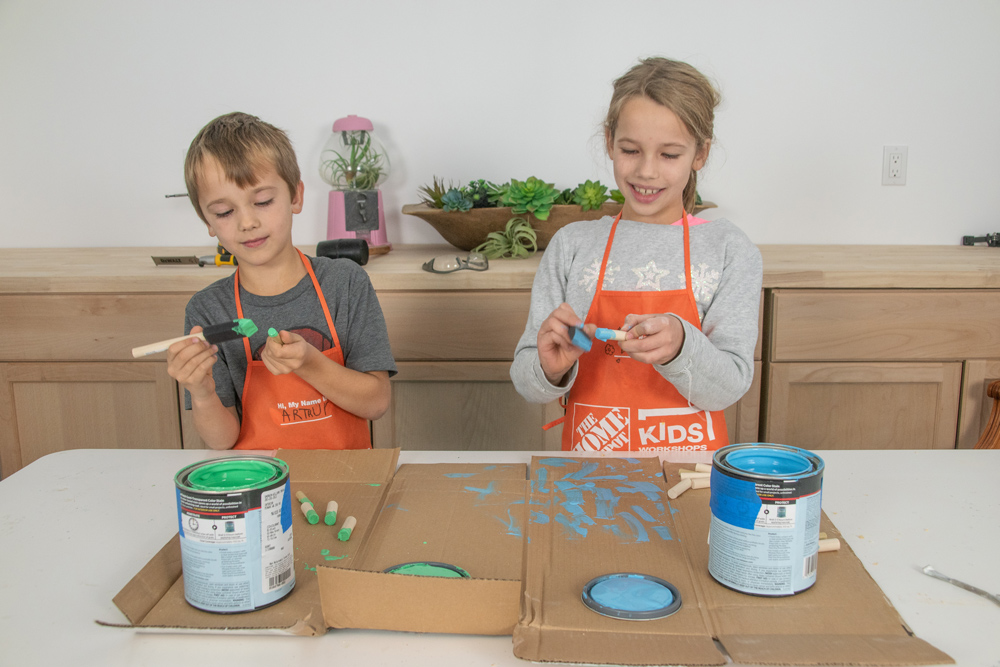 Two children painting dowels with green and blue paint.