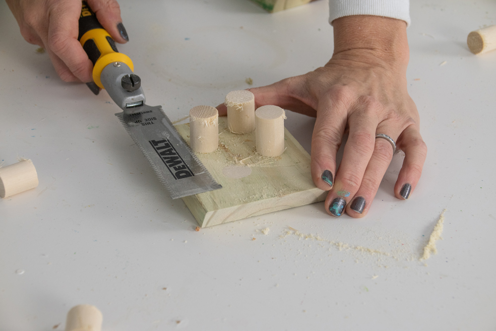A woman’s hand using a pull saw to cut dowels flush to a piece of wood.