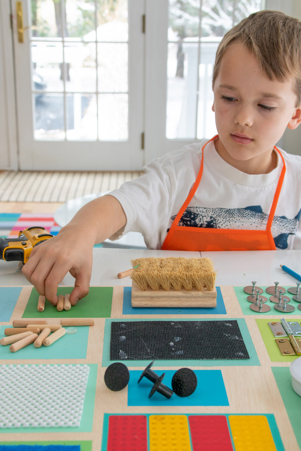 A boy picking up dowel pins on a DIY sensory board.