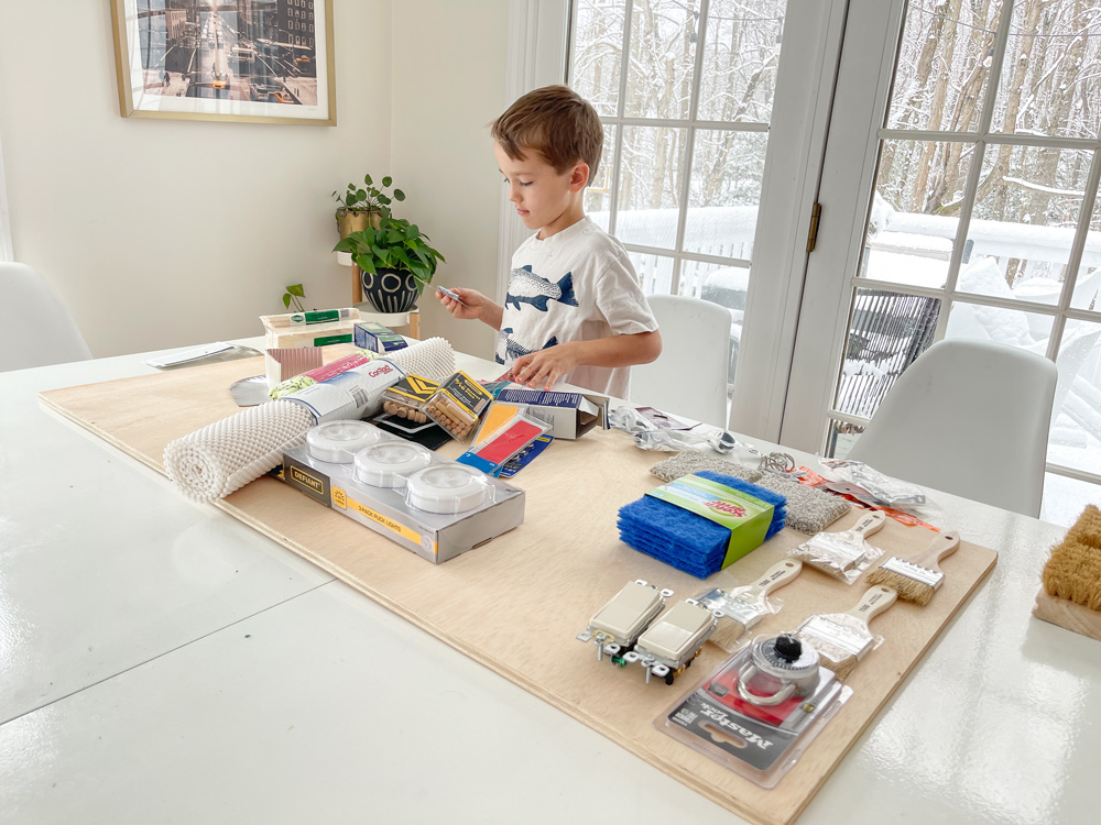 A child standing at a table overlooking supplies needed to create a DIY sensory board.