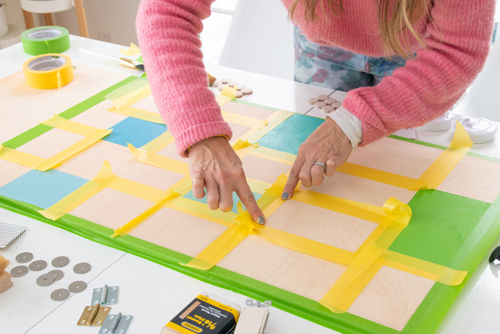 A woman’s hands applying yellow painter’s tape to a wooden board.
