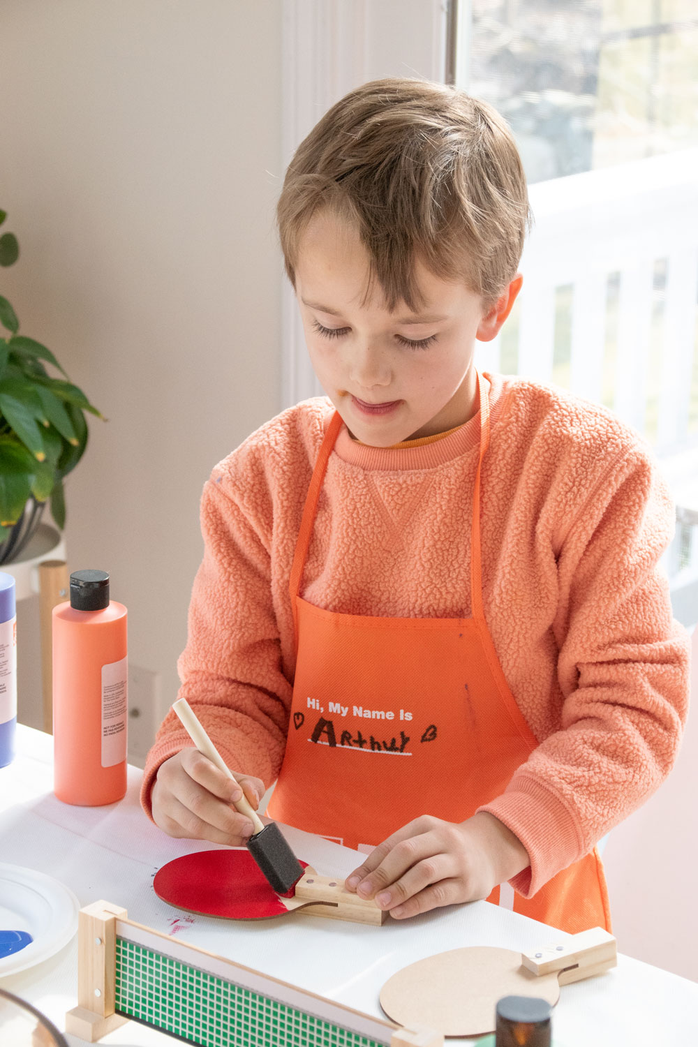 A boy painting a table tennis mallet with red paint.