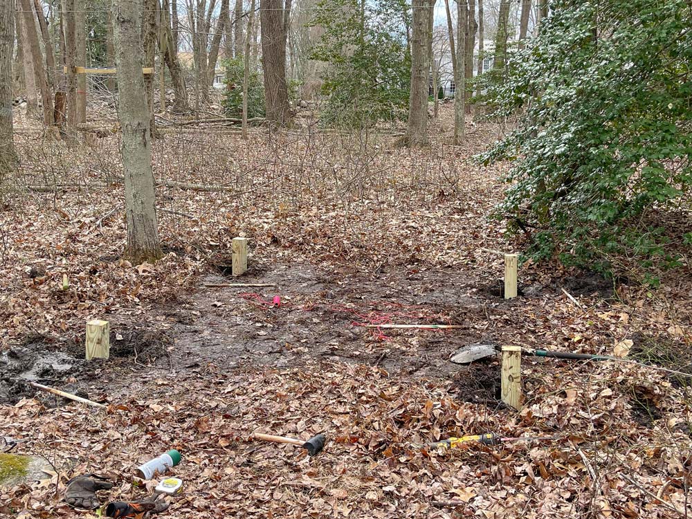 A cleared area in the woods with four posts in the ground.