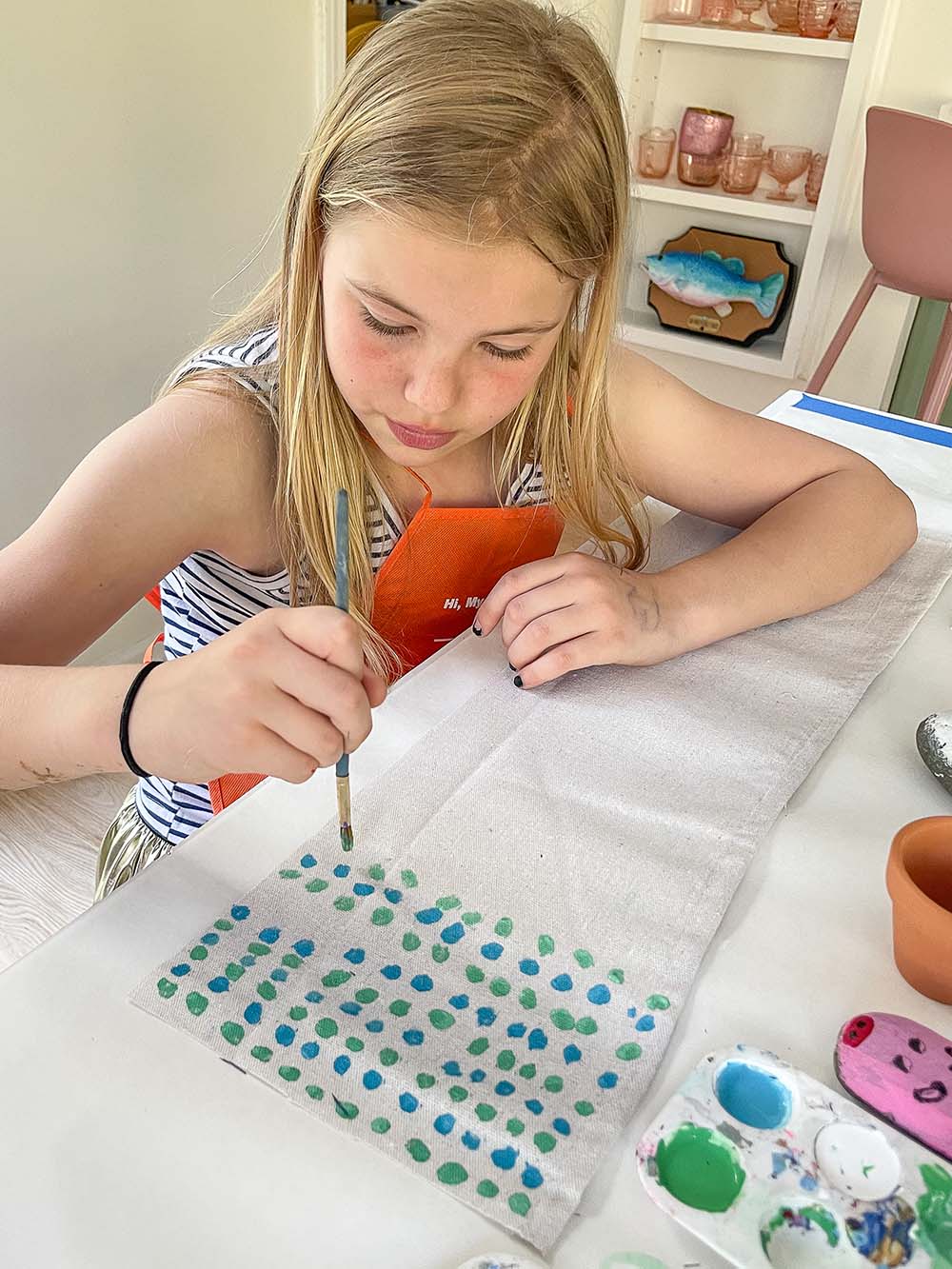 A child painting blue and green dots on a long piece of cloth.