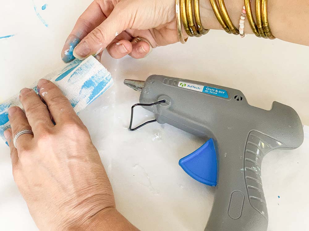 A woman hot gluing the ends of the painted cloth together to form a pillow case.