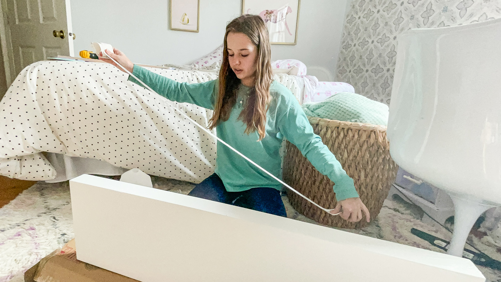 Girl measuring the length of a floating shelf.