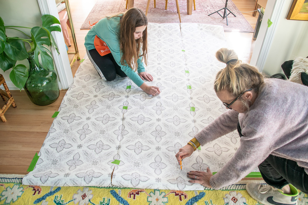 Mother and daughter on the floor measuring and marking on a wallpaper.