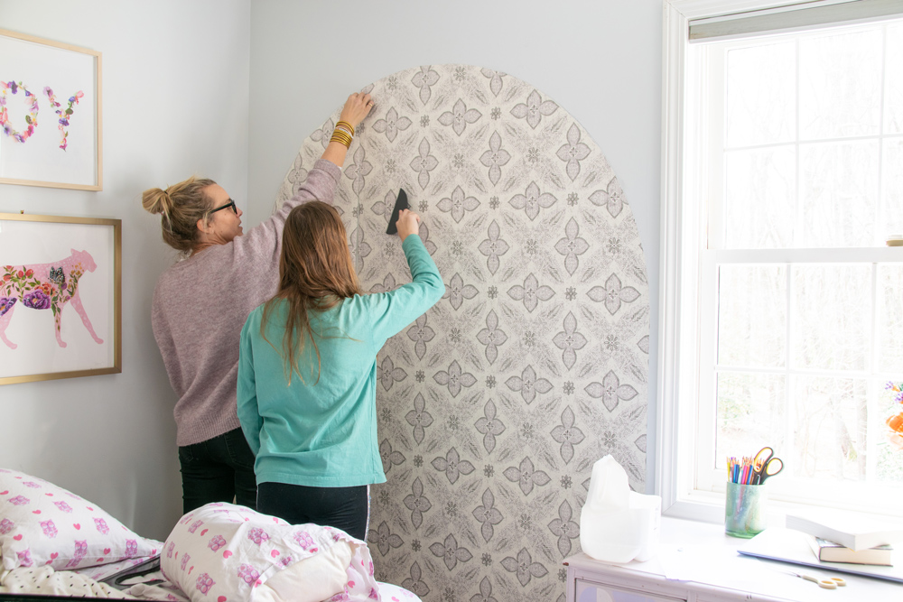 Mother and daughter smoothing wallpaper onto the wall.
