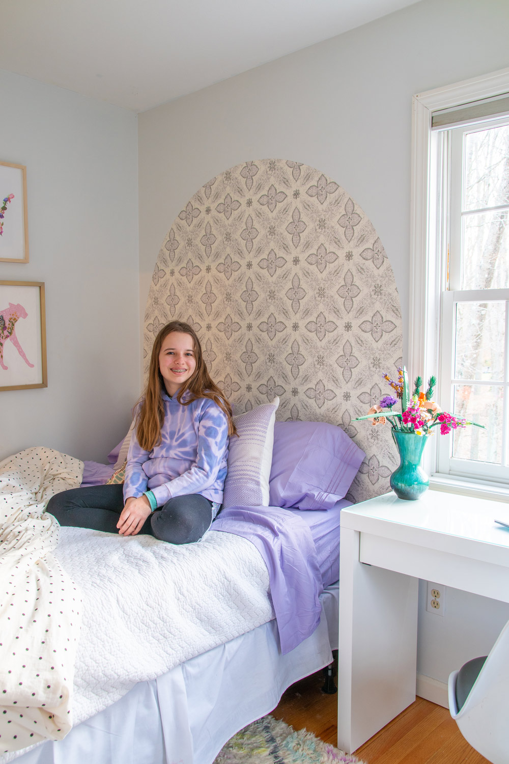 Girl sitting on her bed with wallpaper headboard.