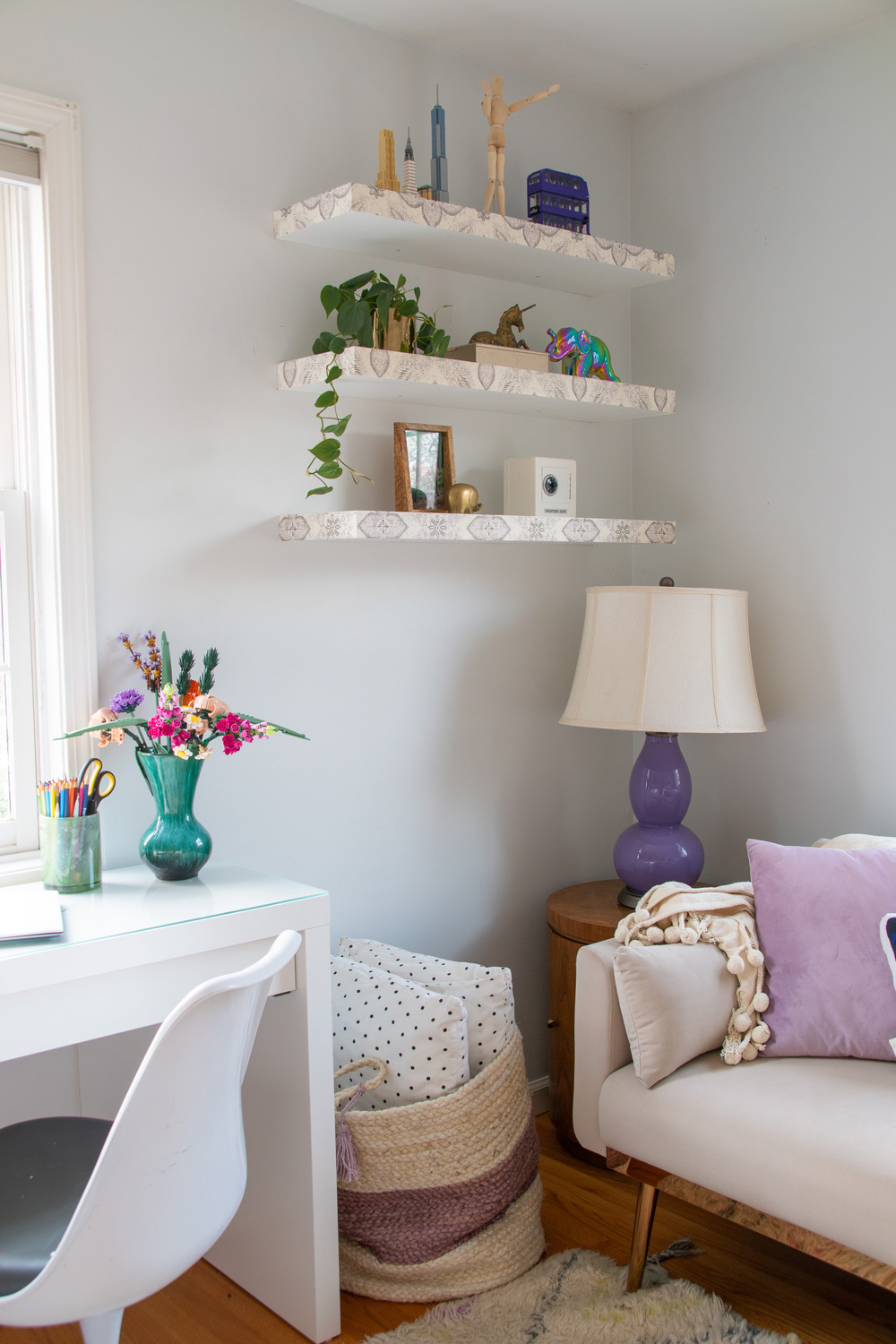 Decorated floating shelves, basket, and loveseat with purple and butterfly throw pillow.