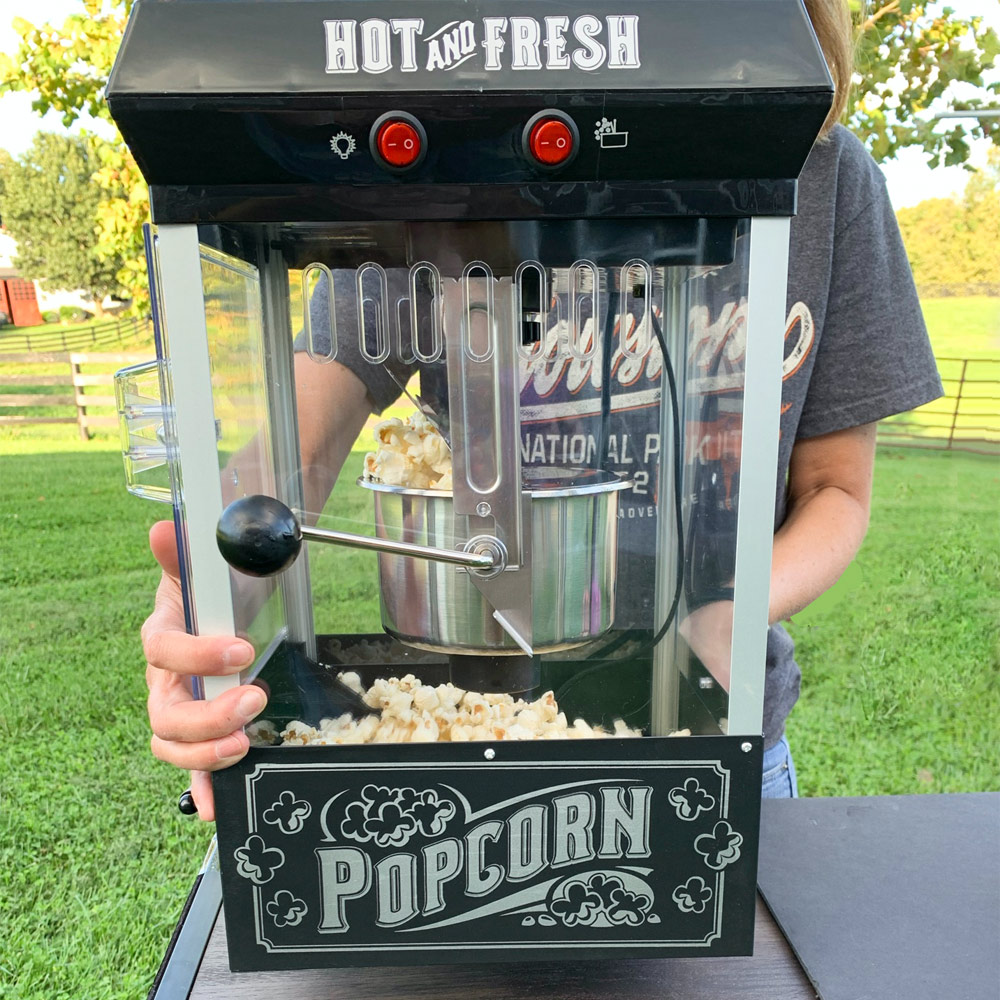 Person standing behind concession stand with popcorn machine and custom candies.