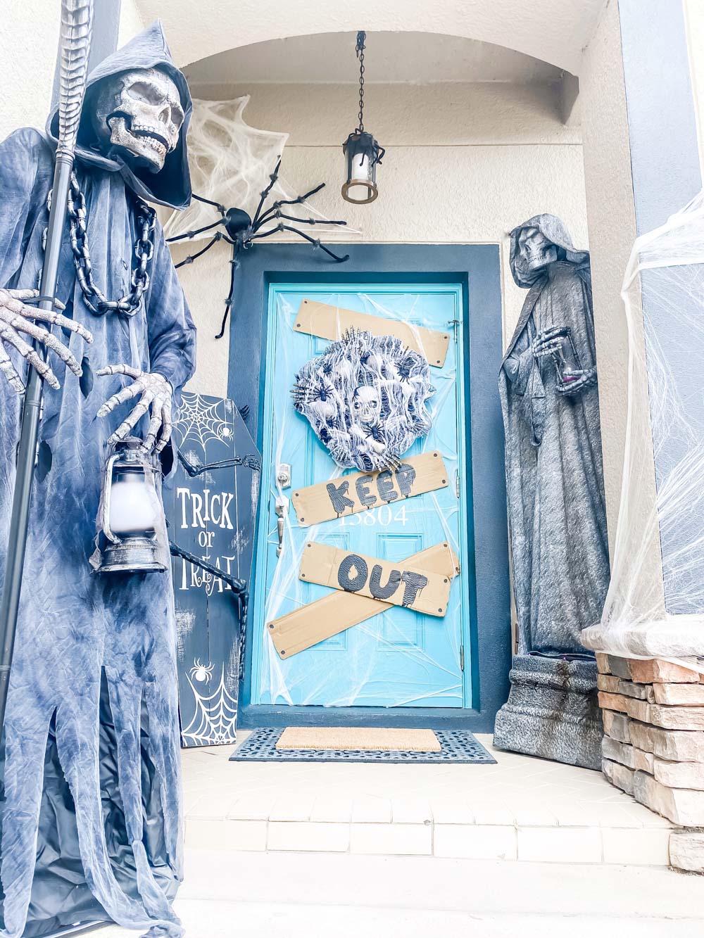 A spooky Halloween front porch guarded by a grim reaper and cemetery statue.