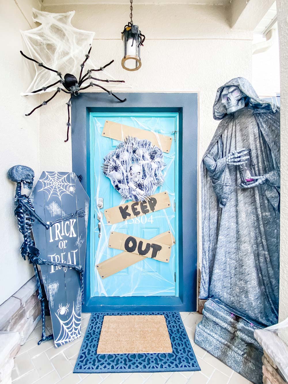 A spooky cemetery front porch for Halloween decorated with spiders and a cemetery statue. 