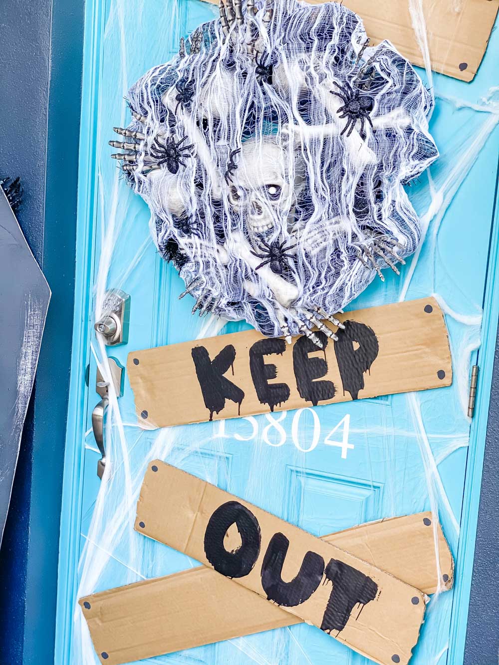 A blue front door decorated with a spooky skeleton wreath and a keep out sign.