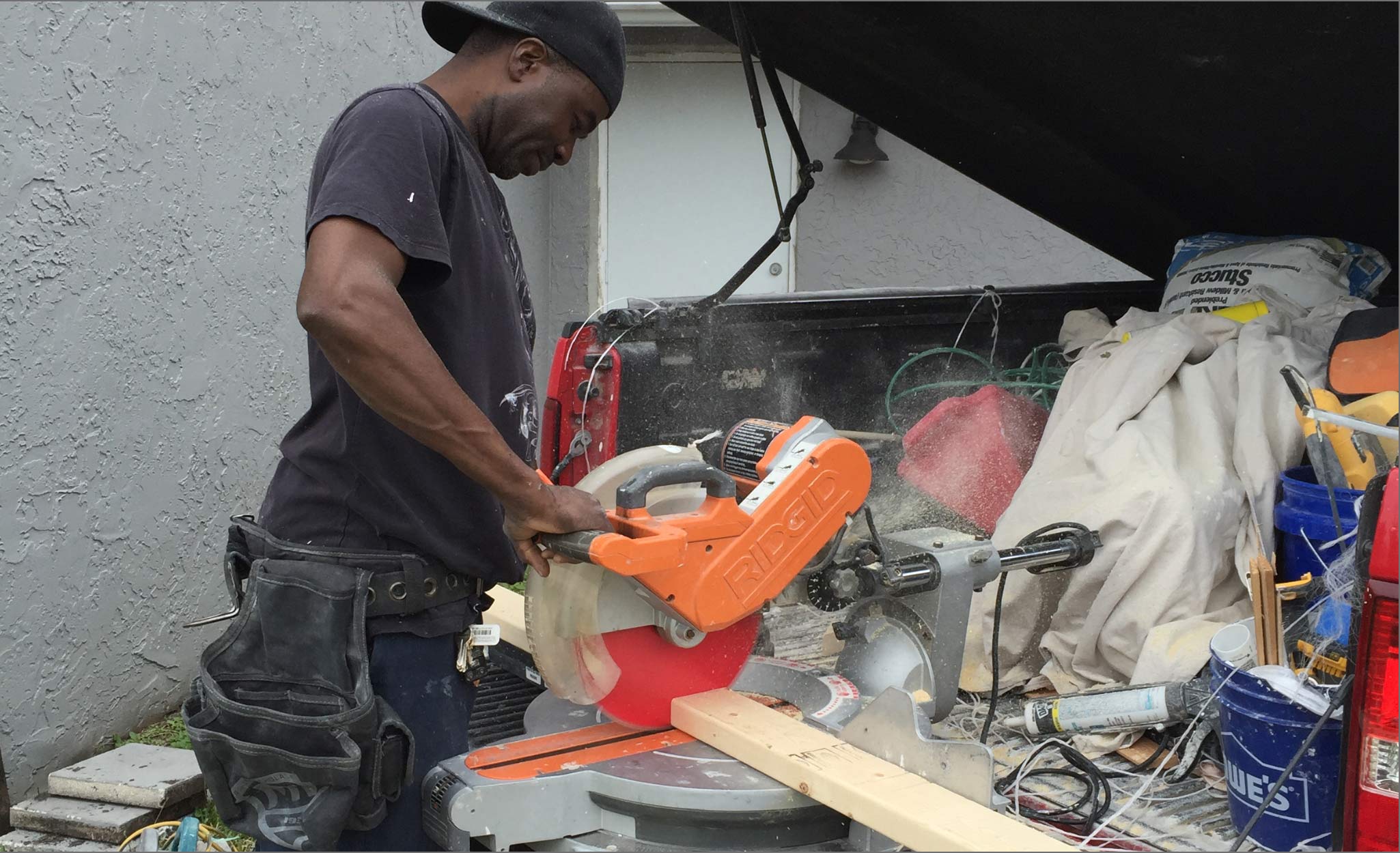 A man cuts a board at the back of a truck.